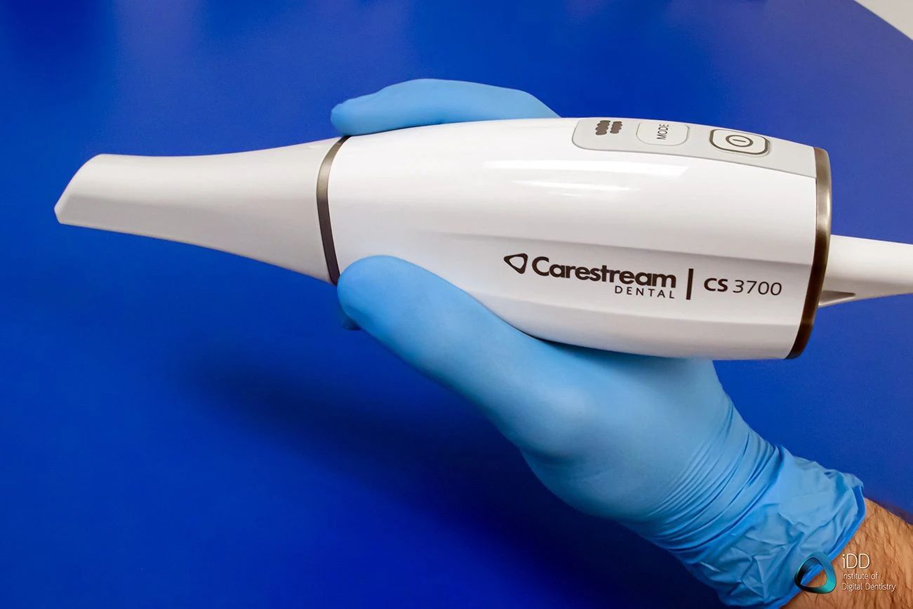 A gloved hand holding a Carestream CS 3700 dental imaging device